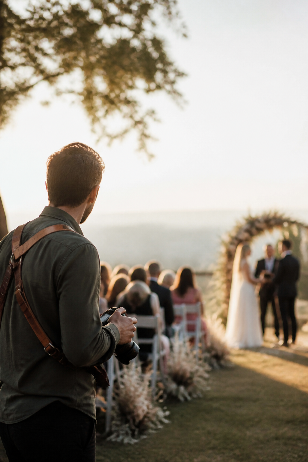 Un photographe en retrait pendant une cérémonie de mariage, appareil à la main, dans une lumière de fin d'après-midi